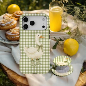 May include: A phone case and pop socket with a white goose illustration, green bow, and boots on a green and white gingham background. The image also shows a glass of yellow liquid, lemons, and pastries.