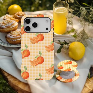 Puede incluir: Una funda de teléfono y un soporte pop con un diseño de acuarela de naranja sobre un patrón de cuadros amarillos. La imagen también incluye un vaso de zumo de naranja, un limón y pasteles.