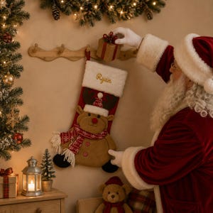May include: A red and tan Christmas stocking featuring a plush reindeer character wearing a red and white patterned scarf and a matching hat. The stocking has a white faux fur cuff with the name Ryan embroidered in gold script lettering.