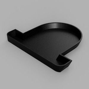 Puede incluir: Una bandeja negra en forma de L con una superficie texturizada. La bandeja presenta una sección redondeada y un compartimento rectangular más pequeño. El diseño es minimalista y moderno, adecuado para organizar objetos pequeños.
