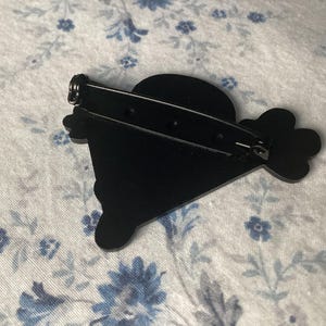 Pu&ograve; includere: Una spilla nera dal design unico, con una parte superiore arrotondata e una forma stilizzata con un elemento a forma di fiore. La spilla ha una chiusura di sicurezza sul retro per un fissaggio sicuro. Questo &egrave; probabilmente un accessorio di moda.