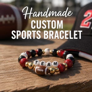 May include: A handmade custom sports bracelet with red, black, white, and gold beads. The bracelet spells out "TEAM" with white letter beads and features a football charm. The image also shows a football and a baseball cap.
