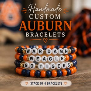 May include: Stack of four handmade custom Auburn bracelets. Each bracelet features a combination of orange, navy blue, and gold beads. White letter beads spell out phrases. The bracelets are stacked on a wooden surface.