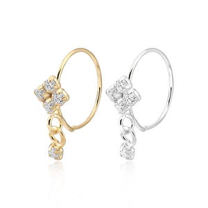 Puede incluir: Dos piercings de nariz, uno dorado y otro plateado, cada uno con un grupo de cuatro piedras con eslabones colgantes y una sola piedra. La joyería se presenta sobre un fondo blanco, resaltando el brillo de las piedras.