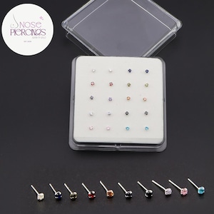 Peut inclure: Un ensemble de piercings de nez avec des pierres précieuses de différentes couleurs. Les piercings sont présentés dans un étui en plastique transparent avec un insert en mousse blanche. Des clous de nez individuels avec des gemmes de couleurs variées sont également visibles.