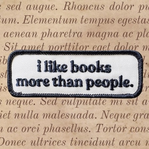 Può includere: Una toppa rettangolare con sfondo bianco e bordo nero. La toppa presenta la frase ricamata "i like books more than people" in nero, perfetta per gli amanti dei libri e della lettura.