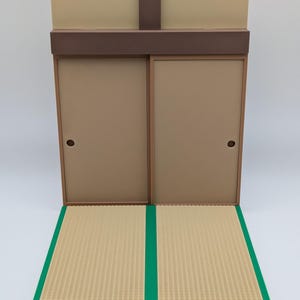 Könnte beinhalten: Ein Miniatur-Diorama eines japanischen Zimmers mit Schiebetüren und einem Tatami-Mattenboden. Die Wände sind beige und braun, und der Boden hat eine gewebte Textur mit grünen Zierleisten. Für kleine Figuren oder Sammlerstücke.