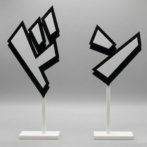 Puede incluir: Dos esculturas abstractas. Cada una tiene una forma geométrica blanca con bordes negros, montada sobre un tallo y una base blancos. Una se asemeja a un puño, la otra a una flecha estilizada. El fondo es gris liso.