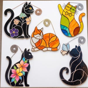 May include: Five stained glass cat ornaments with metal chains. One black cat with floral patterns, one yellow cat with a bow tie, one orange and white cat, one black cat with pink and yellow flowers, and one black cat with a light blue butterfly.