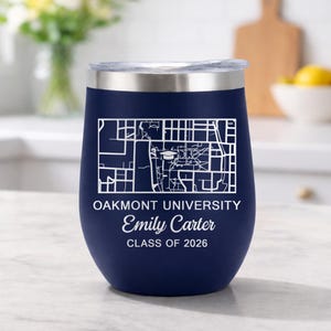 May include: A navy blue insulated tumbler with a silver rim and lid. The tumbler features a white map design and text that reads "Oakmont University", "Emily Carter", and "Class of 2026".