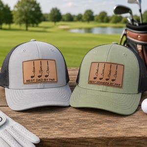 May include: Two golf-themed trucker hats. One is gray with a black mesh back, the other is olive green with a black mesh back. Both have a brown leather patch with golf clubs and the text "BEST DAD BY PAR" and "BEST GRANDPA BY PAR".