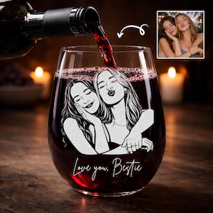 May include: Stemless wine glass with a custom illustration of two women, with the words "Love you, Bestie" in script. The glass is filled with red wine, and a bottle is pouring more wine into the glass.