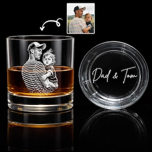 May include: A clear whiskey glass with a photo of a man and child etched on the front. The glass is filled with amber liquid. The lid of the glass has the words "Dad & Tom" in white script.