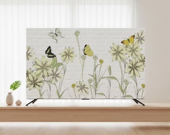May include: A flat-screen TV with a floral and butterfly design. The artwork features yellow and green flowers, butterflies, and a brick-like background. The TV is on a light wood table, with a small vase and decorative ball.