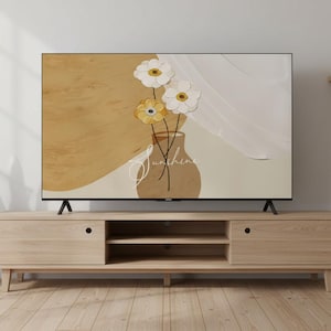 Op de afbeelding: Een tv-scherm toont een bloemenkunstprint. Het kunstwerk toont een vaas met witte en gele bloemen, met het woord "Sunshine" in script. De tv staat op een licht houten mediaconsole met twee deuren en open schappen.