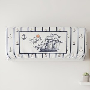 May include: White air conditioning unit cover with a navy blue nautical theme. The cover features a central panel with a detailed illustration of a sailing ship and the text "You can everything". Vertical navy stripes and anchor motifs.