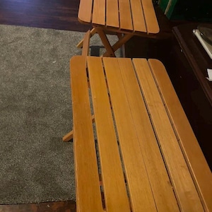 May include: Two wooden folding tables with a natural finish. The tables have a rectangular top made of wooden slats and a folding leg design. One table is positioned above the other.