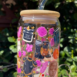 May include: A clear glass tumbler with a bamboo lid and a glass straw. The tumbler is decorated with stickers of pink roses, books, boots, and the text "Should I Get The Wingleader?" and "Not Today".