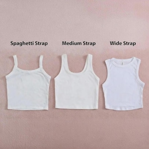 May include: Three white cropped tank tops displayed side by side. The left top is labeled Spaghetti Strap, the middle top is labeled Medium Strap, and the right top is labeled Wide Strap. Each top features a different shoulder strap width.