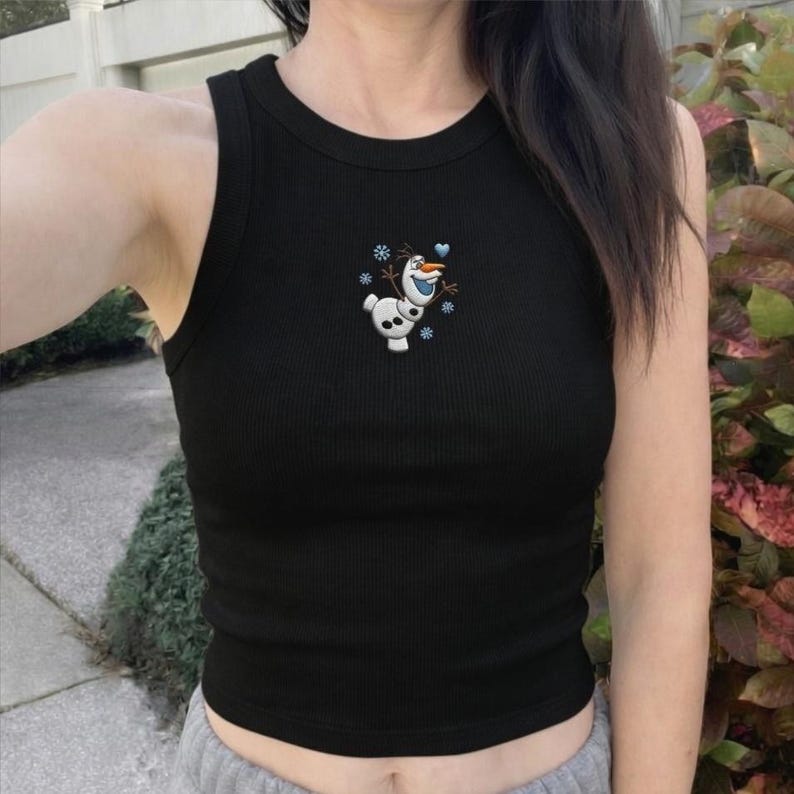 May include: Black ribbed tank top with a small embroidered Olaf design. The design features the snowman character with snowflakes and a blue heart. The tank top is sleeveless and has a round neckline.