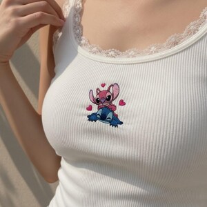 Peut inclure: D&eacute;bardeur blanc c&ocirc;tel&eacute; avec une encolure en dentelle. Le d&eacute;bardeur pr&eacute;sente un motif brod&eacute; d'un personnage de dessin anim&eacute; rose et bleu avec des c&oelig;urs.
