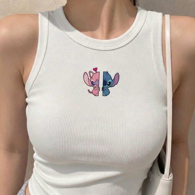 May include: A white ribbed tank top featuring a small embroidered graphic on the chest. The graphic depicts two split cartoon characters, one pink and one blue, with a small red heart positioned above the pink character's head.
