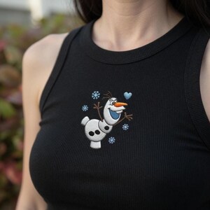 May include: Black ribbed tank top featuring an embroidered Olaf design from the movie Frozen. The design includes a smiling snowman with a carrot nose, blue heart, and snowflakes. The tank top has a rounded neckline and sleeveless design.