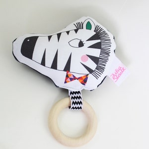 May include: A black and white zebra rattle with a colorful bow tie and a wooden ring. The rattle has a pink nose and green eyes. The tag says "Julia Staute".