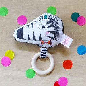 May include: A black and white zebra-shaped baby rattle with a wooden ring. The rattle has a bow tie and the text "Bulla Stante" on the side.