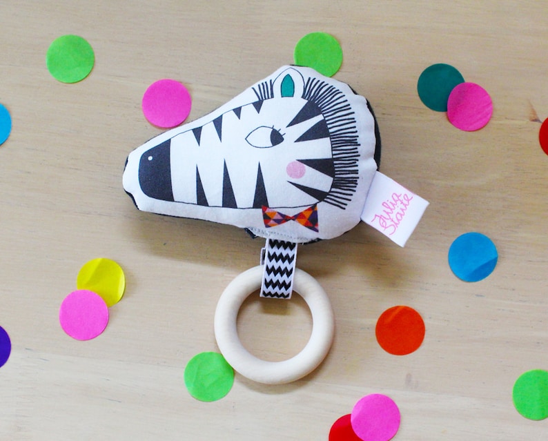 May include: A black and white zebra-shaped baby rattle with a wooden ring. The rattle has a bow tie and the text "Bulla Stante" on the side.