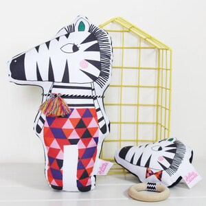 May include: Two black and white zebra plush toys with colorful geometric patterns. The larger zebra is standing upright and the smaller zebra is lying down. Both toys have the text "Silly Jane" on them.