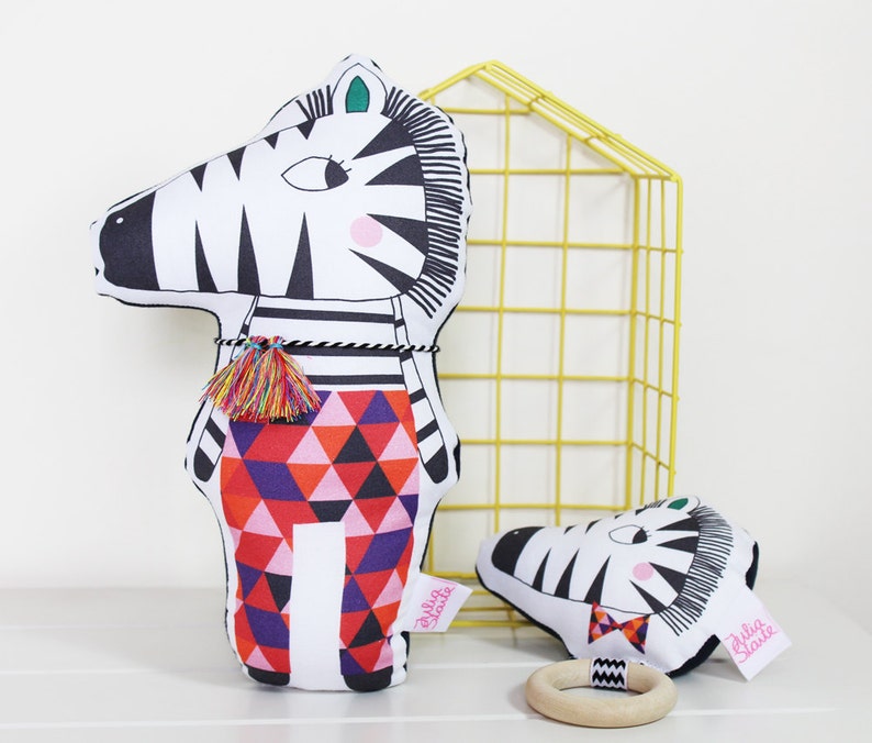 May include: Two black and white zebra plush toys with colorful geometric patterns. The larger zebra is standing upright and the smaller zebra is lying down. Both toys have the text "Silly Jane" on them.