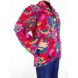 May include: A red quilted jacket with a vibrant paisley pattern in shades of pink, blue, green, and yellow. The jacket features gold buttons and blue trim. The sleeves have a puffed design.