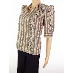 May include: A vintage blouse with a patterned design. The blouse features a V-neckline, short sleeves, and a mix of vertical stripes and dotted patterns in beige, black, and pale purple. The sleeves have a slight puff at the shoulders.