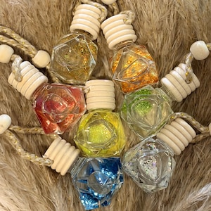 May include: A collection of colorful, faceted glass bottles filled with glitter and liquid, each with a wooden cap and a decorative rope. The bottles are arranged on a bed of dried, feathery grass, showcasing a rainbow of colors.