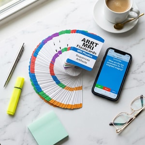 May include: A collection of ARRT MRI Flashcards fanned out next to a smartphone displaying a question about T1-weighted imaging. A cup of coffee, pen, highlighter, sticky note, and glasses are also on the marble surface.