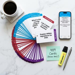 May include: A collection of flashcards fanned out, with blue, red, and purple edges, and a smartphone displaying a medical question. A cup of coffee, a highlighter, and a pen are also present. The flashcards have questions about physical care, psychosocial topics, and CNA roles.