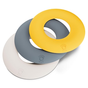 Puede incluir: Tres salvamanteles de silicona en amarillo, gris y blanco roto. Cada salvamanteles es circular con un agujero en el centro y un pequeño logotipo. Estos salvamanteles resistentes al calor protegen las superficies.