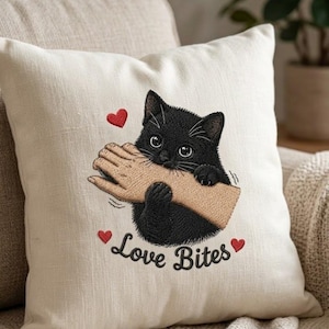May include: Cushion in cream fabric featuring an embroidered black cat biting a hand. The text "Love Bites" is embroidered below the cat, with red heart accents.