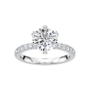 May include: A sparkling engagement ring with a large, round-cut diamond as the centerpiece. The band is made of polished silver and is encrusted with smaller diamonds, creating a halo effect around the main stone. The ring is set against a white background.