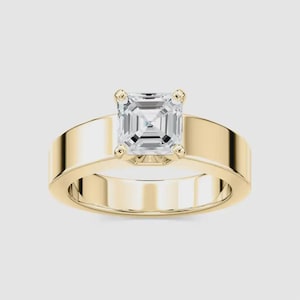 May include: A gold ring with a large, square-cut diamond center stone. The band is wide and smooth, with a polished finish. The diamond is clear and reflects light, creating a sparkling effect. The ring is set against a neutral background.