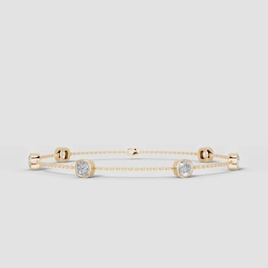 Puede incluir: Una delicada pulsera de cadena de oro con cinco piedras preciosas transparentes de talla cojín, espaciadas uniformemente y engastadas en biseles de oro. La pulsera incluye un pequeño cierre de mosquetón en el centro que une los eslabones.