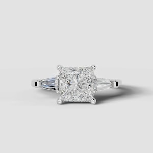 May include: A silver-toned ring featuring a large, square-cut center stone held by four prongs. On each side of the center stone, there is a single, elongated, tapered baguette-cut stone set horizontally into the polished metal band.