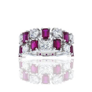 May include: A silver-toned ring featuring an alternating pattern of rectangular-cut deep pink stones and round-cut clear stones. The band is wide and set with multiple rows of these faceted gems, creating a continuous, symmetrical, and sparkling design.