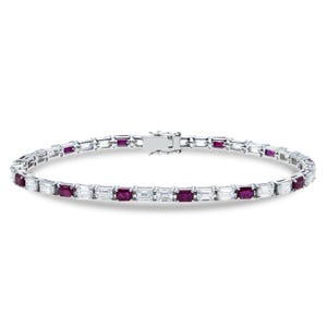 Puede incluir: Una pulsera de tenis en tono plateado que presenta un patrón alterno de rubíes de color rojo intenso con corte rectangular y piedras blancas transparentes con corte baguette. La pulsera se asegura con un cierre de caja metálico.