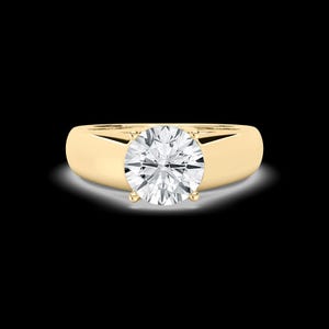 May include: A gold ring with a large, round, clear diamond center stone. The ring has a simple, smooth band. The diamond is held in place by four prongs. The ring is set against a black background.