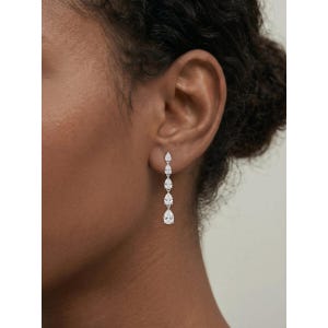May include: Dangling earrings with five clear, pear-cut gemstones. The earrings are arranged in a vertical line, with the largest stone at the base. The earrings are shown against a person's ear and skin, highlighting the design.