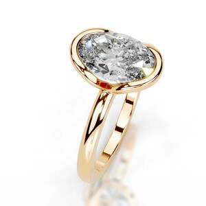May include: A gold ring with a large, oval-cut diamond. The diamond is set in a bezel setting, and the band is smooth and polished. The ring is displayed against a white background, highlighting its sparkle and design.