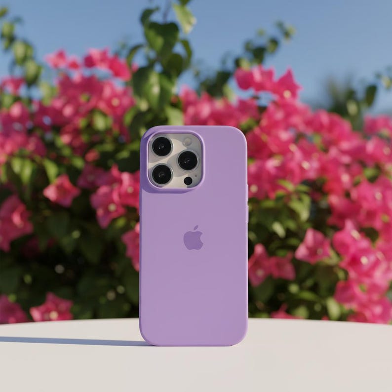 May include: A lavender-colored phone case with a triple-lens camera cutout and the Apple logo. The case is set against a backdrop of vibrant pink flowers and a clear blue sky.