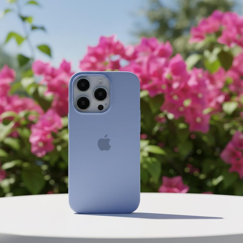 May include: A light blue iPhone case with a triple-lens camera and the Apple logo. The case is on a white surface, with a backdrop of vibrant pink flowers and green foliage under a clear blue sky.